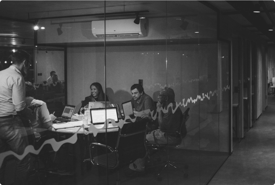 photo of a group of people siting around a desk through a glassdoor inside an office space